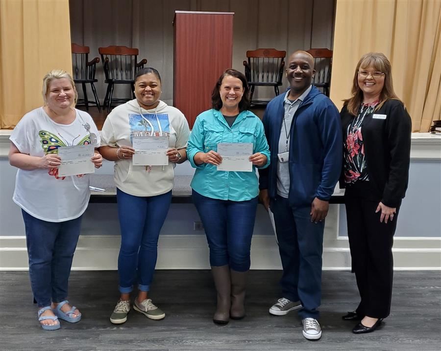 Four teachers pose with a member of the Arc of North Talladega. Three of the teachers each hold a check.